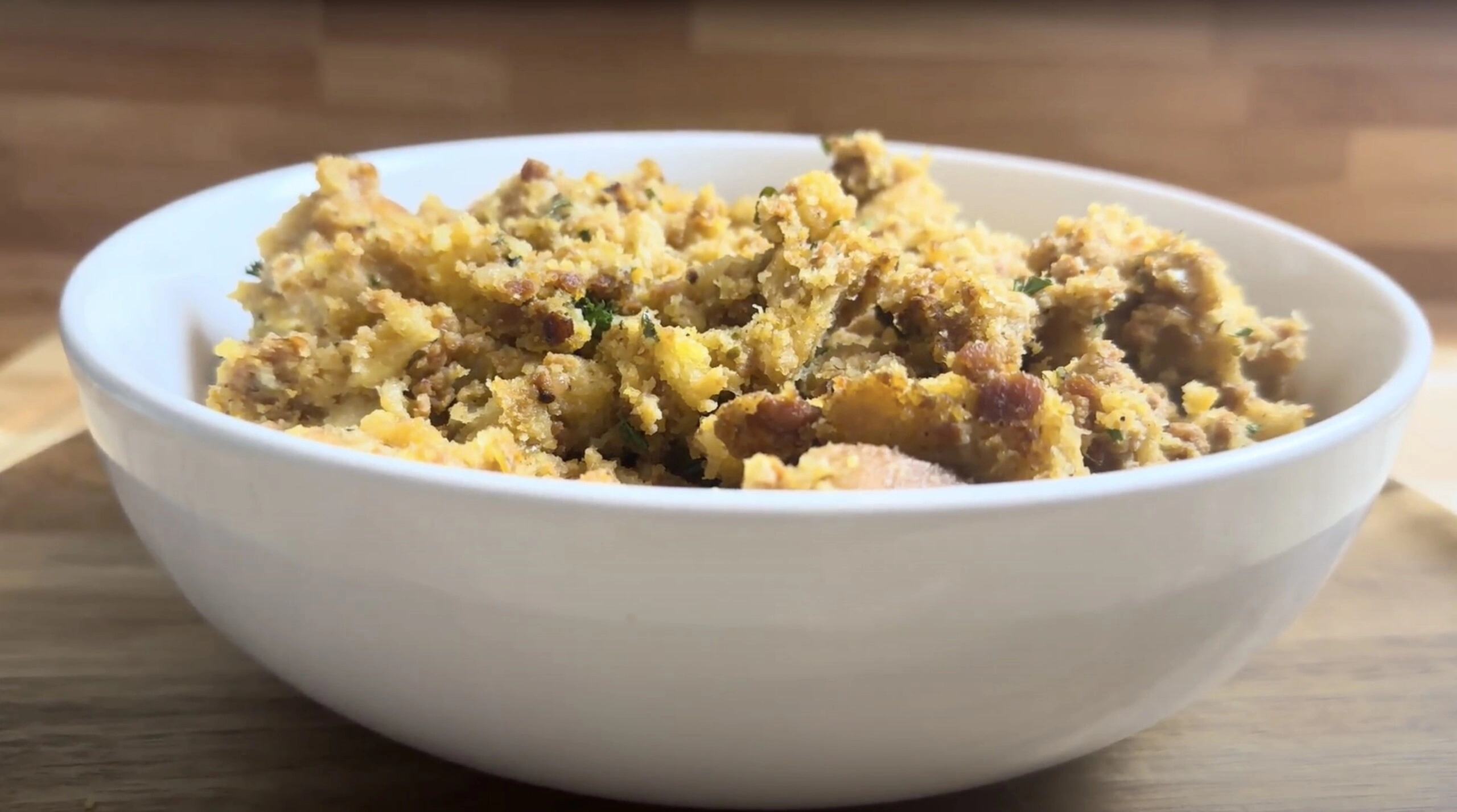 Bowl of homemade cornbread stuffing with herbs on a wooden table.
